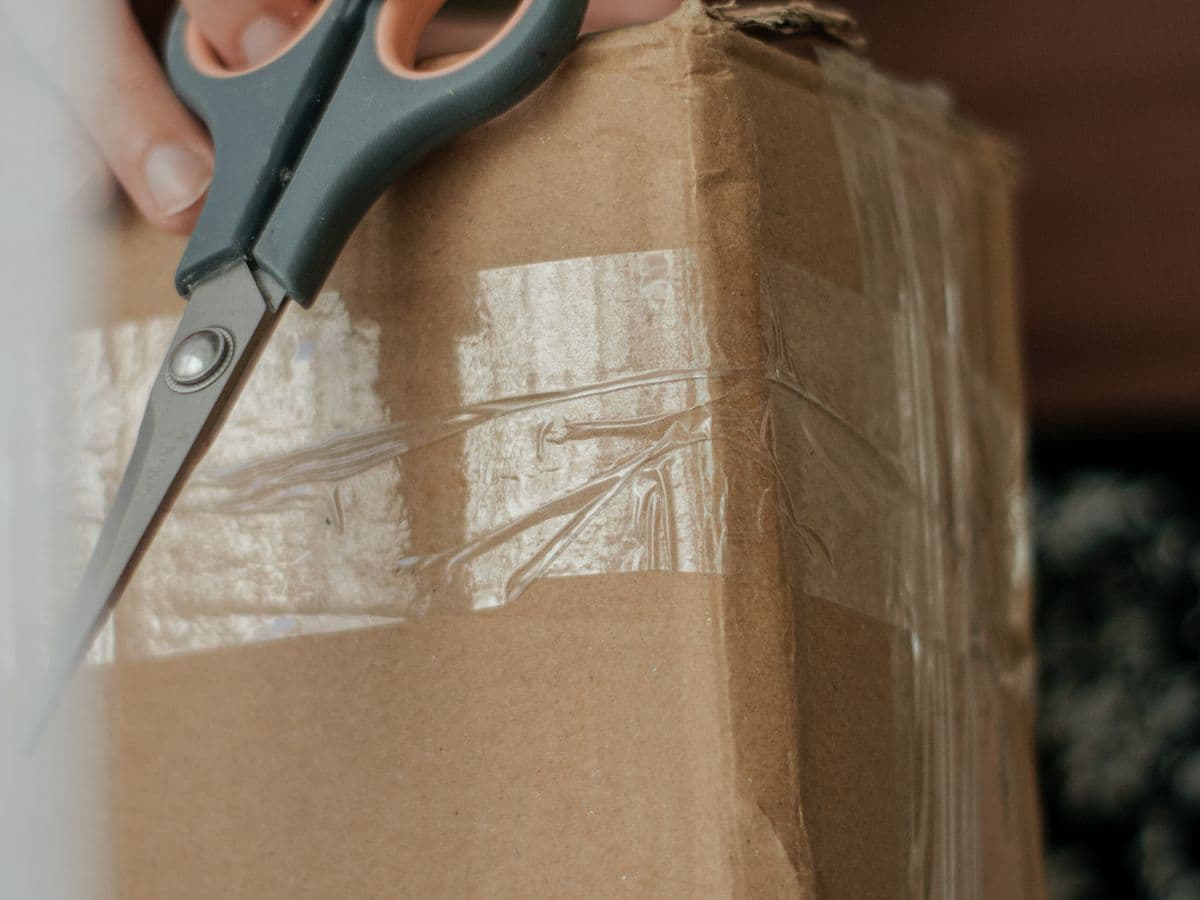 Hand cutting through layers of packing tape on a worn cardboard box
